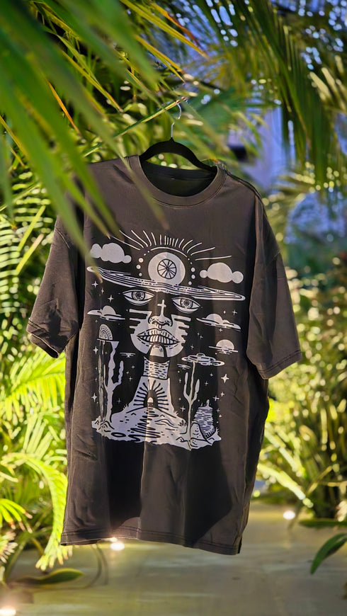 Black t-shirt with white graphic design on a hanger against a natural background